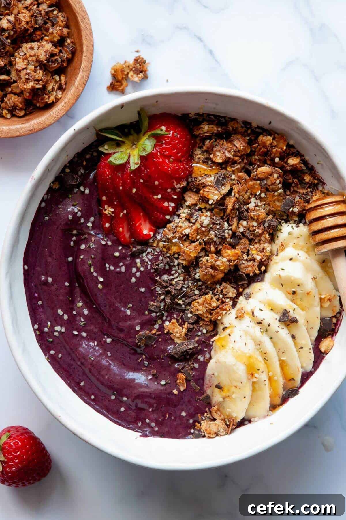 Healthy, high protein acai bowl topped with fresh strawberries, granola, sliced banana, chia seeds, and a honey dipper.