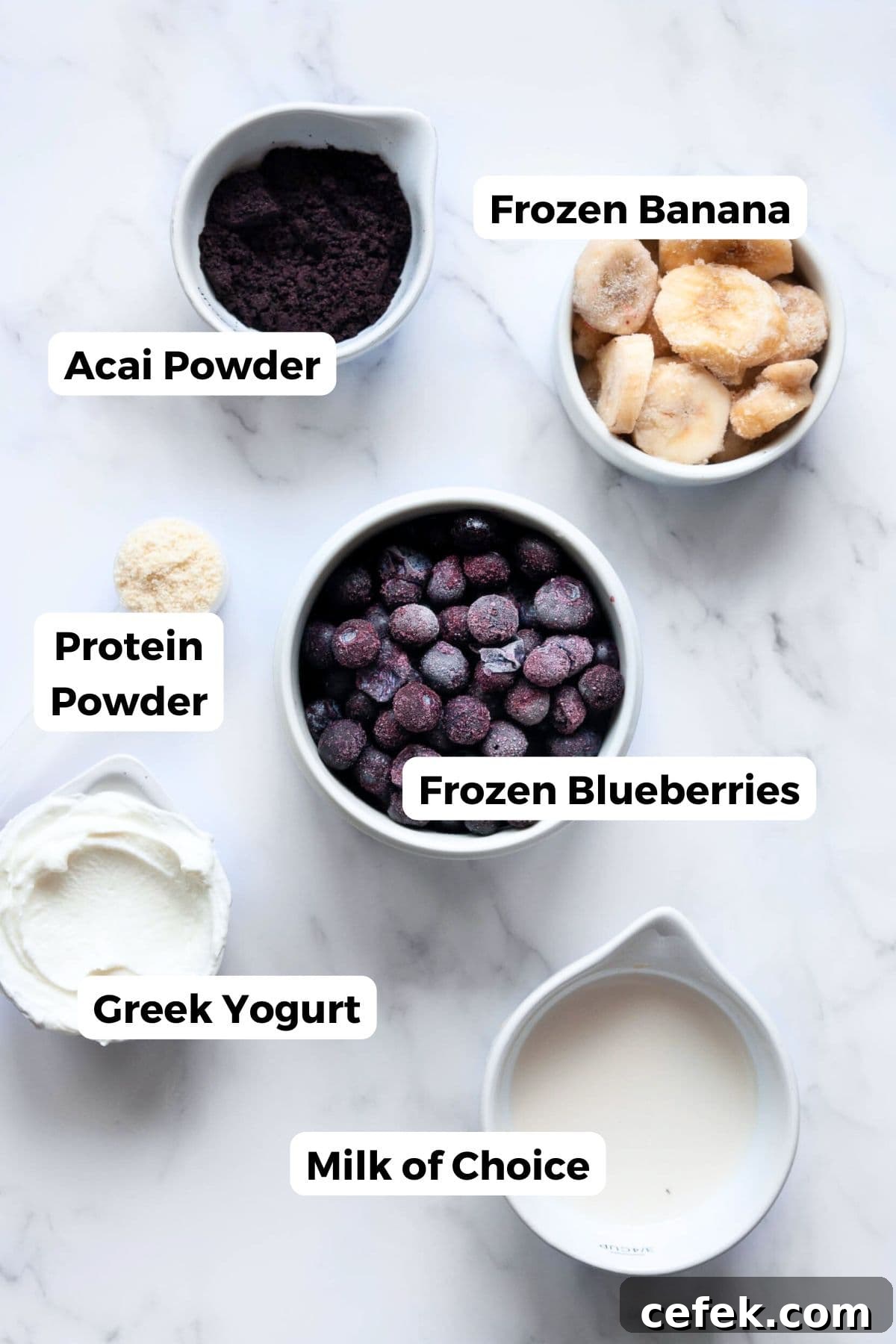 All ingredients in a homemade high-protein acai bowl labeled, including: frozen banana, mixed berries, Greek yogurt, vanilla protein powder, acai powder, and milk of choice.