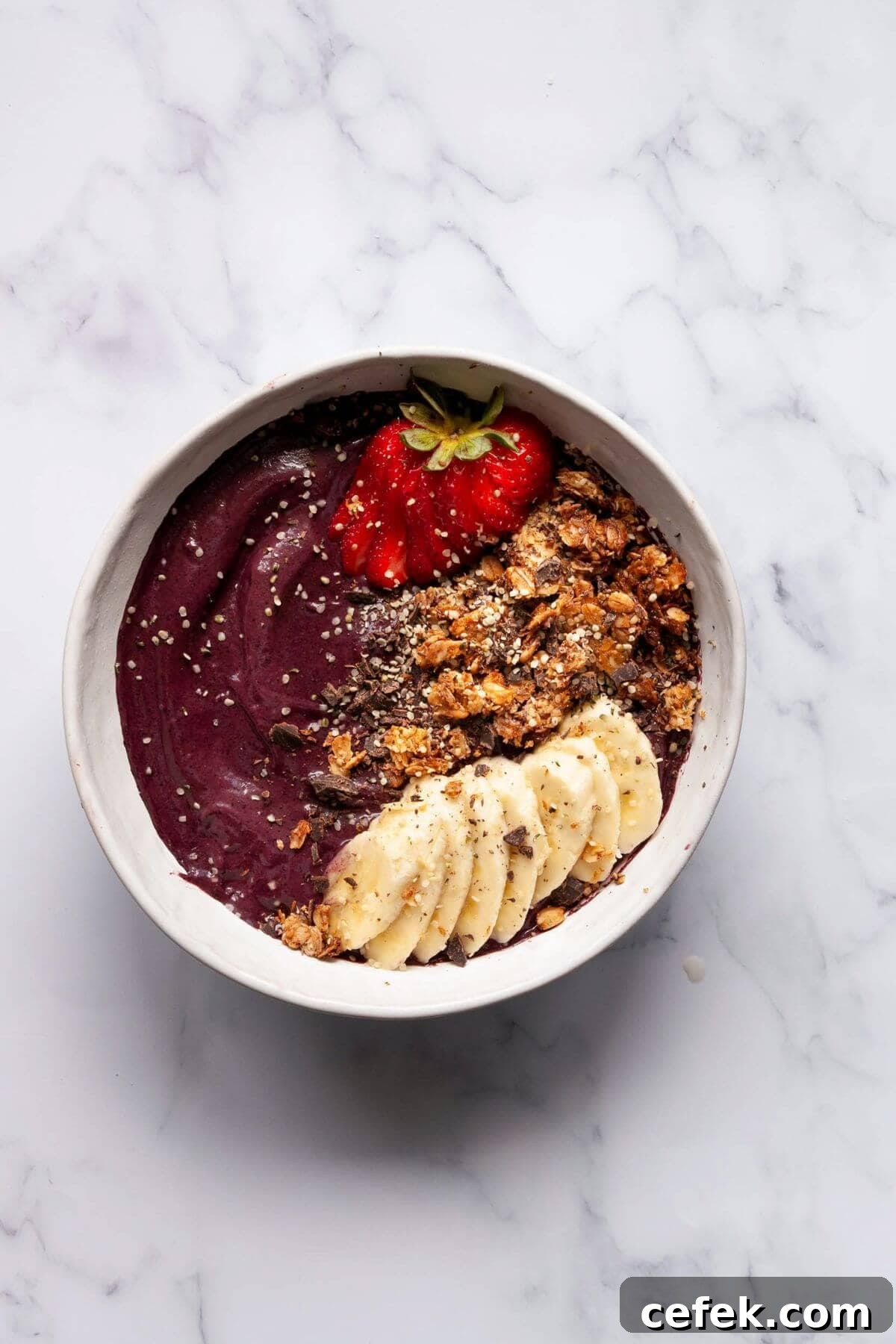 Finished high protein acai bowl in a white bowl topped with strawberries, granola, banana slices, and chia seeds.