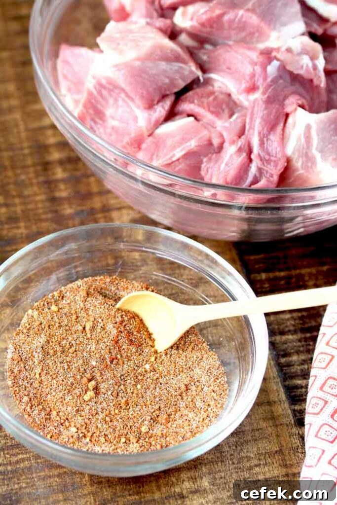 Small glass bowl filled with homemade spice mix next to a bowl of pork cut into big chunks