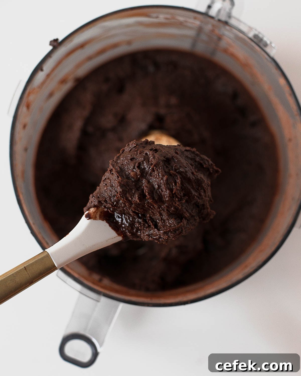Thick chocolate cookie dough made from black beans in a food processor on a spoon