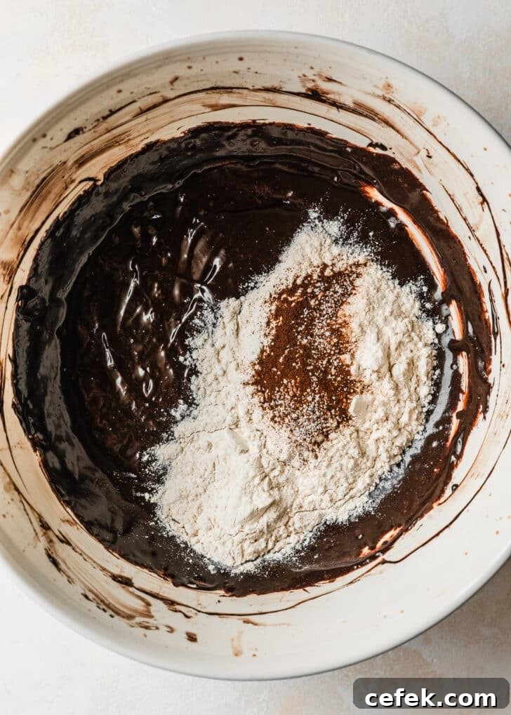 A white bowl of chocolate batter with flour on top.