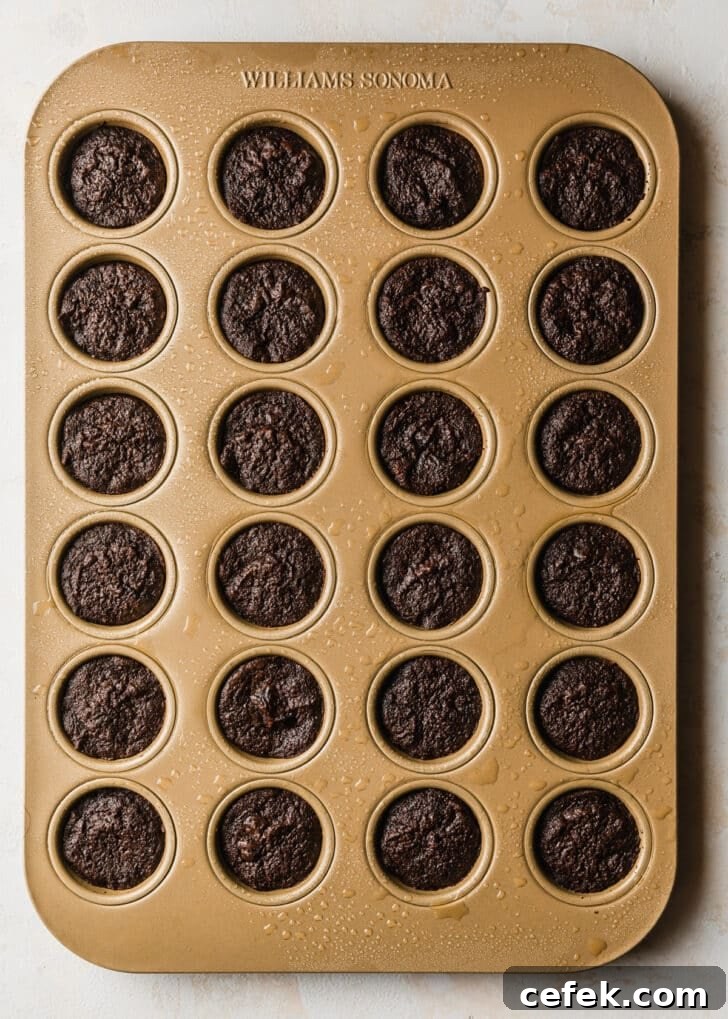 Baked brownie bites in a gold mini muffin tan on a tan counter.