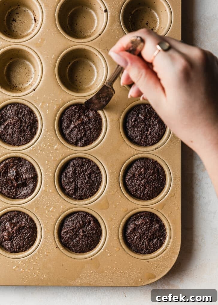 A hand using a butter knife to cut the edges of brownie bites in a gold mini muffin tin.