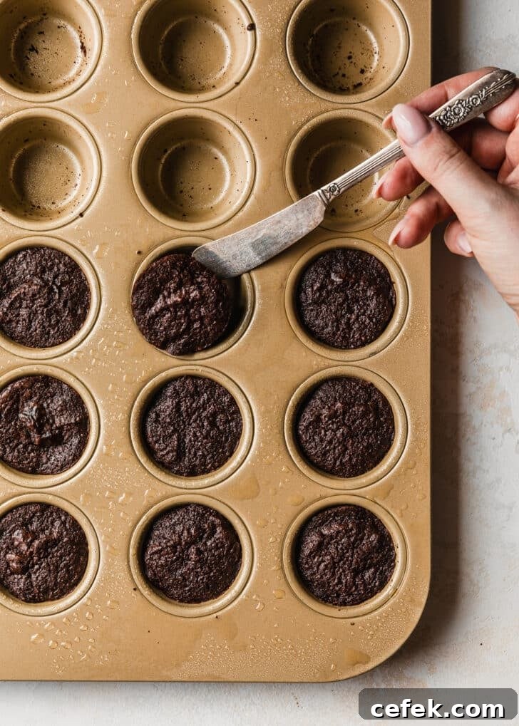 A hand using a butter knife to release brownie bites from a gold mini muffin tin.