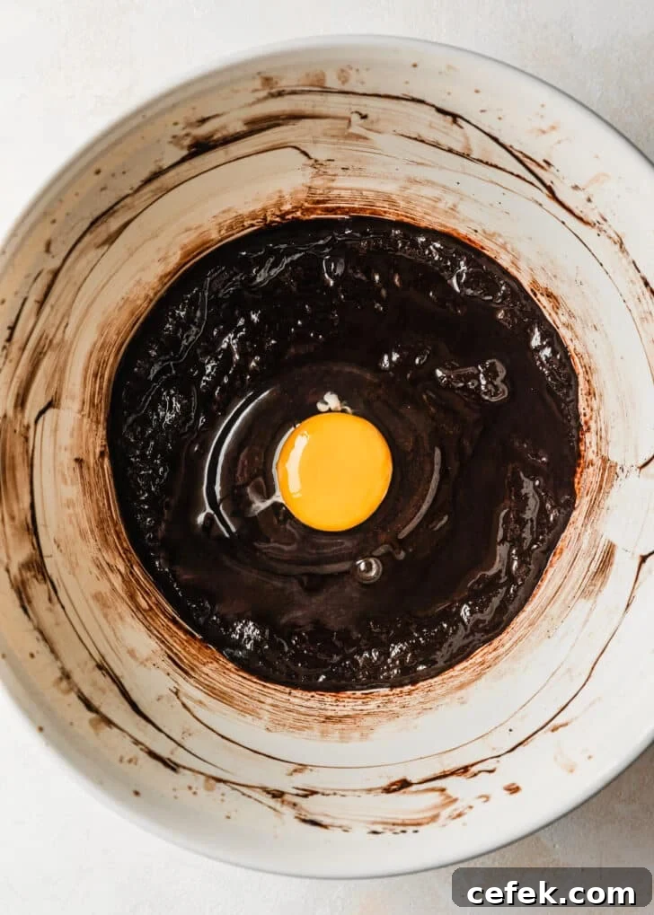 A white bowl of brownie batter with an egg on top.