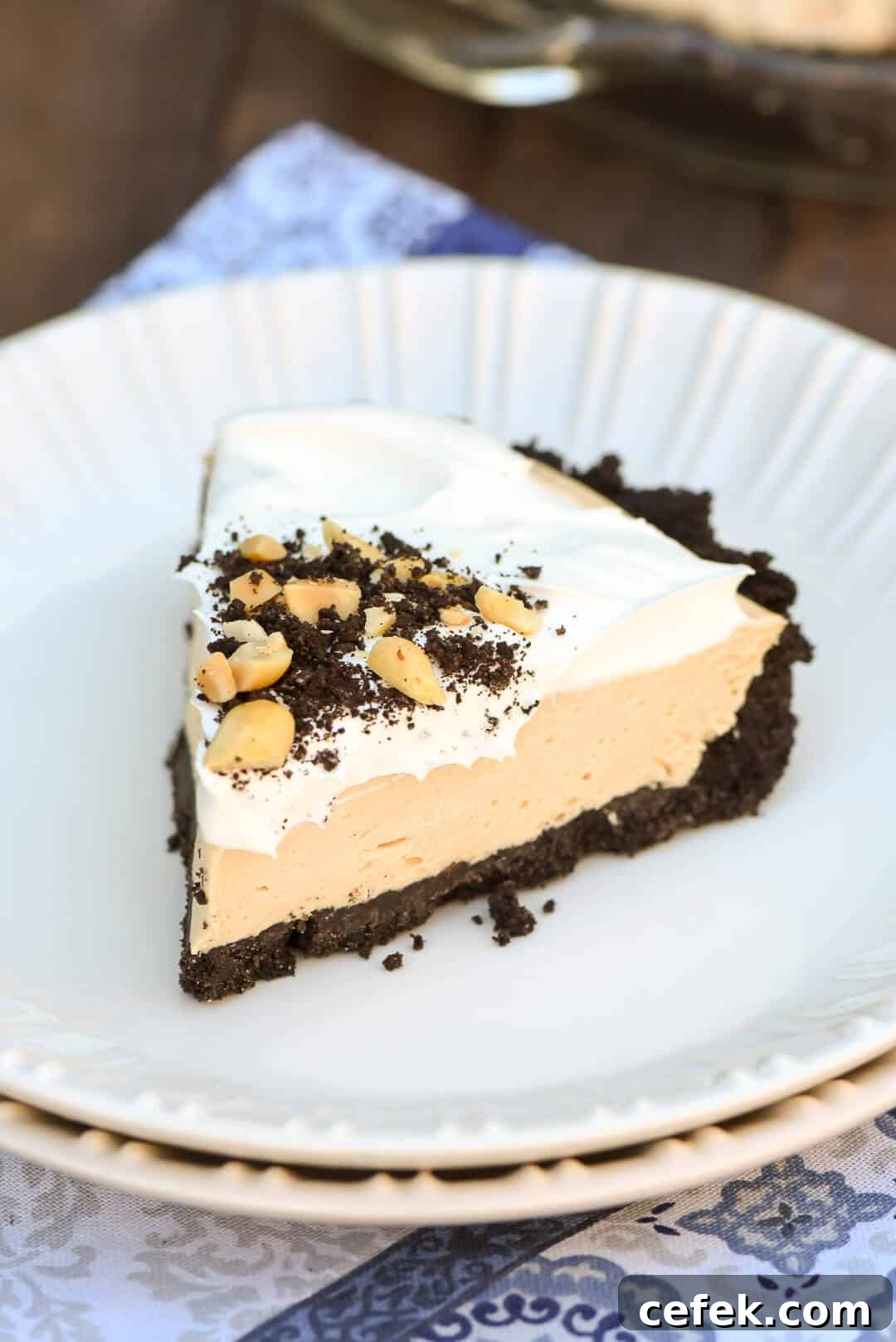 A slice of Frozen Peanut Butter Pie topped with crushed Oreos and peanuts on a white serving plate.