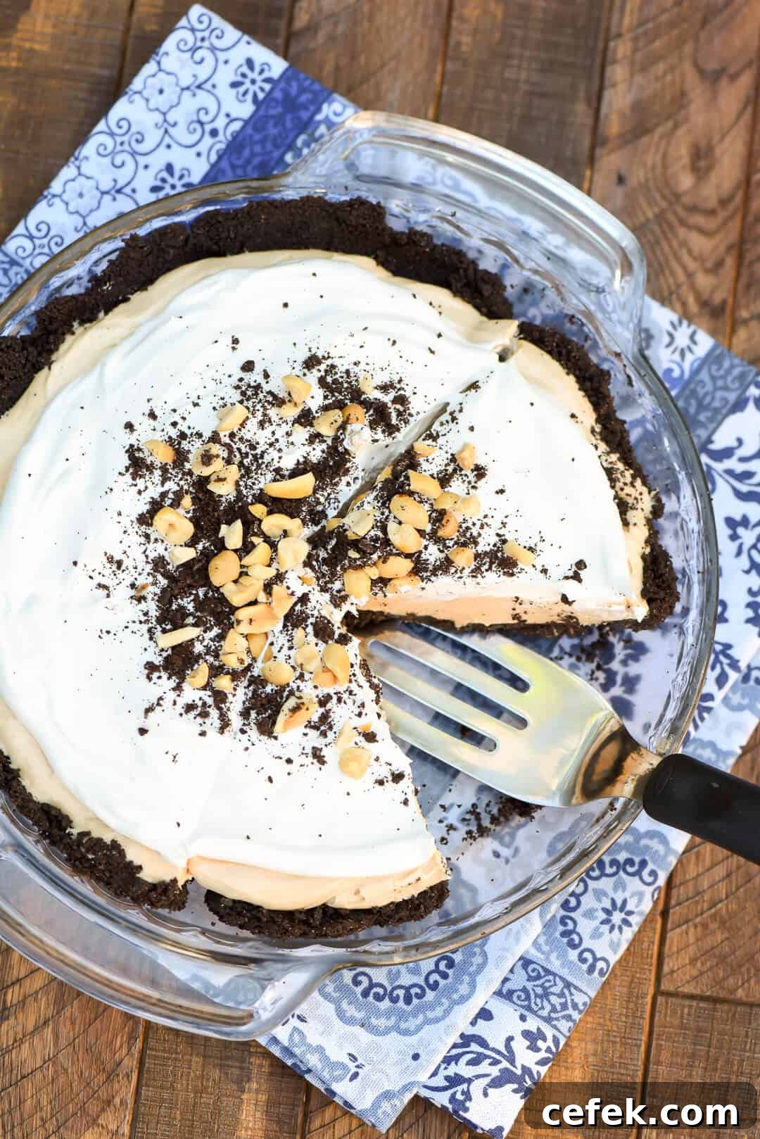 An over the top image showing a spatula lifting a slice of pie from the pie dish that sits on a blue cloth.