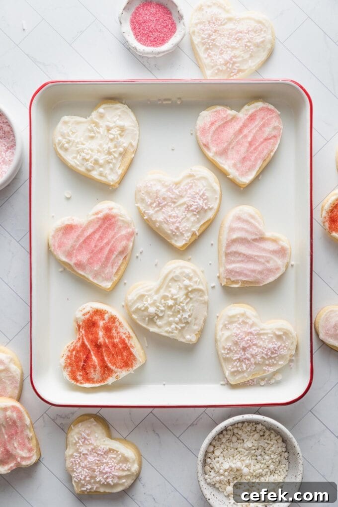Tray filled with heart shaped cut out sugar cookies decorated with spreadable cream cheese cookie frosting and a mix of white, pink, and red sprinkles.