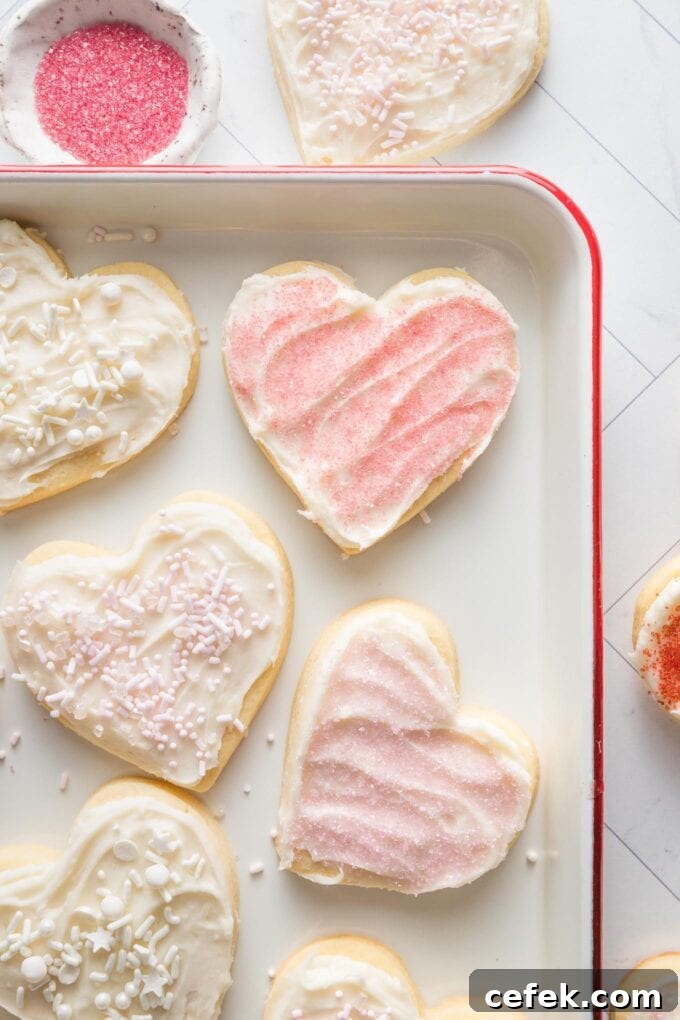 White enamel tray with heart shaped cut out sugar cookies and pink sprinkles in a small pinch bowl nearby.