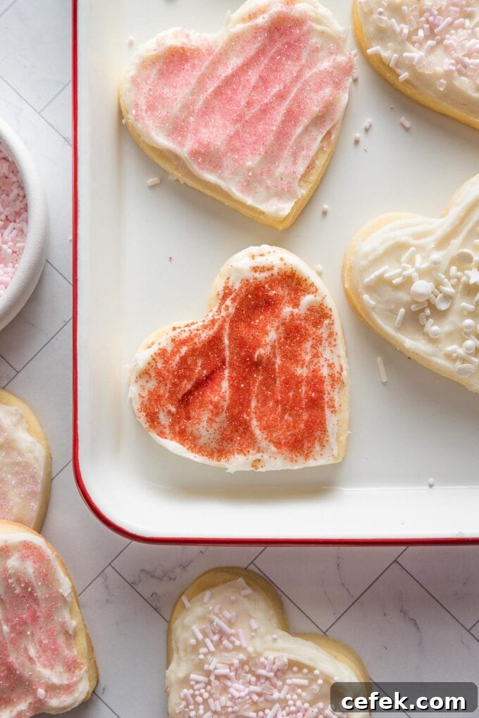 Red sprinkled, frosted heart shaped cut out sugar cookie on a tray, ready to eat.