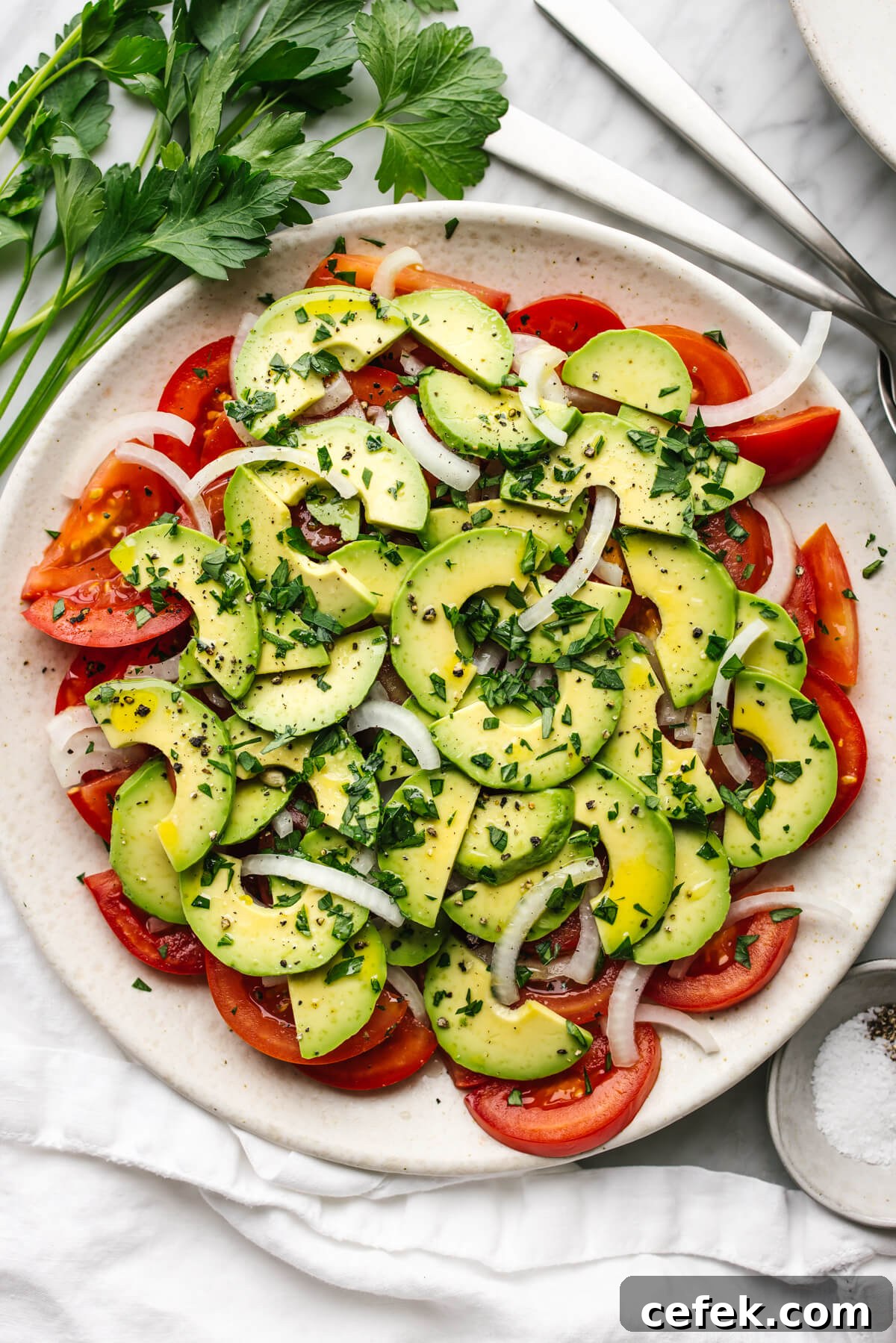 Tomato, onion, avocado salad on a plate next to parsley.