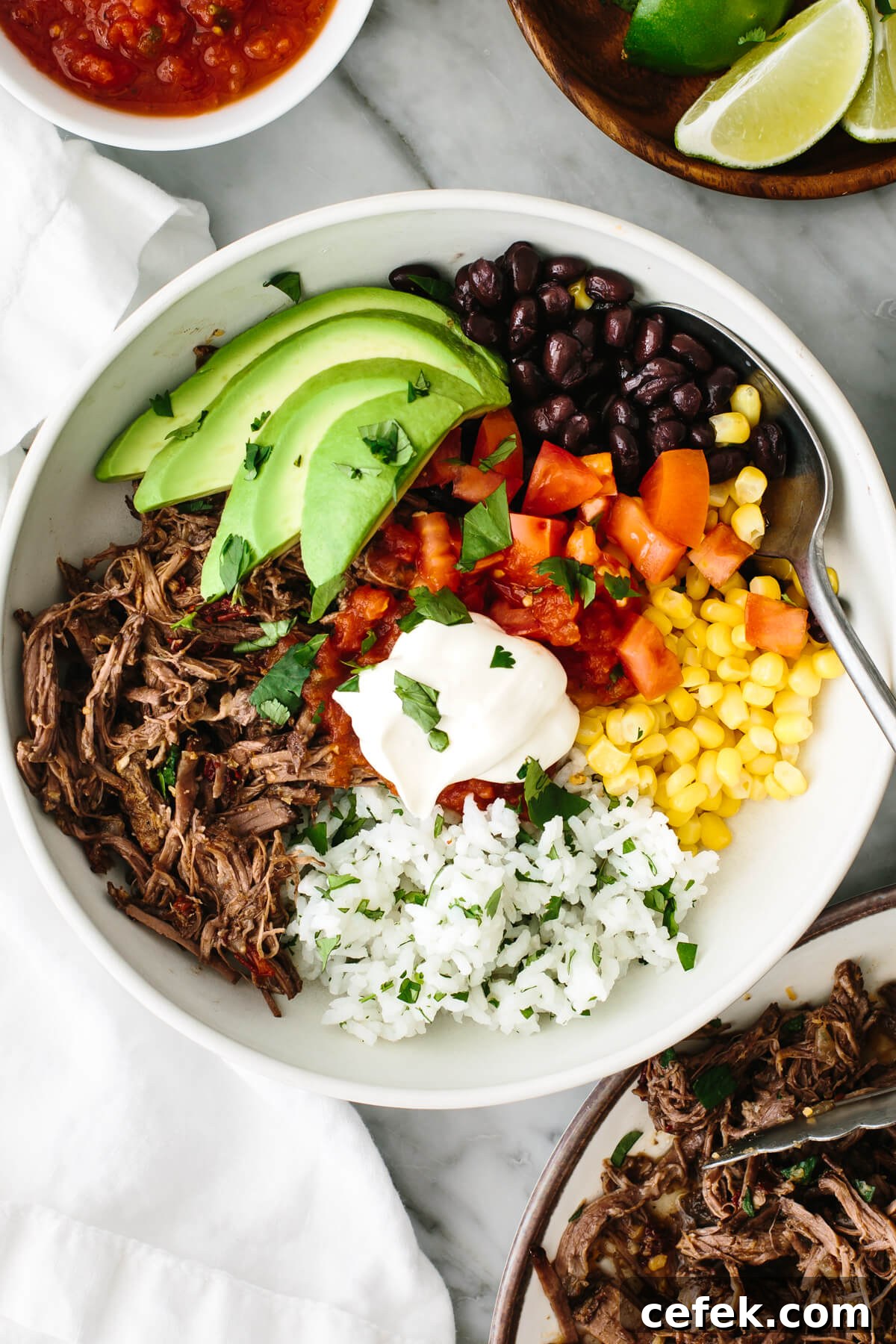 Beef barbacoa burrito bowl on a table with salsa.