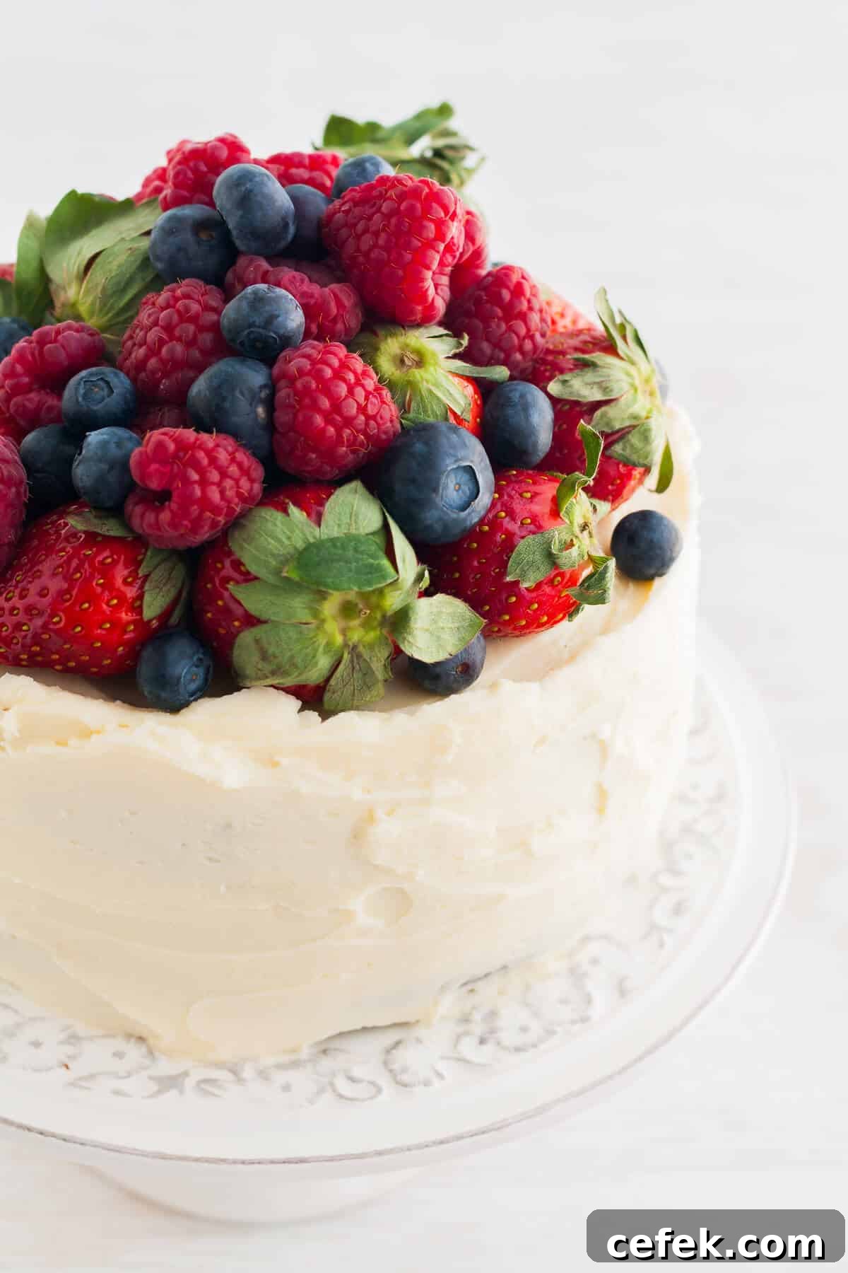 A layer cake topped with a mound of fresh berries on a cake stand.