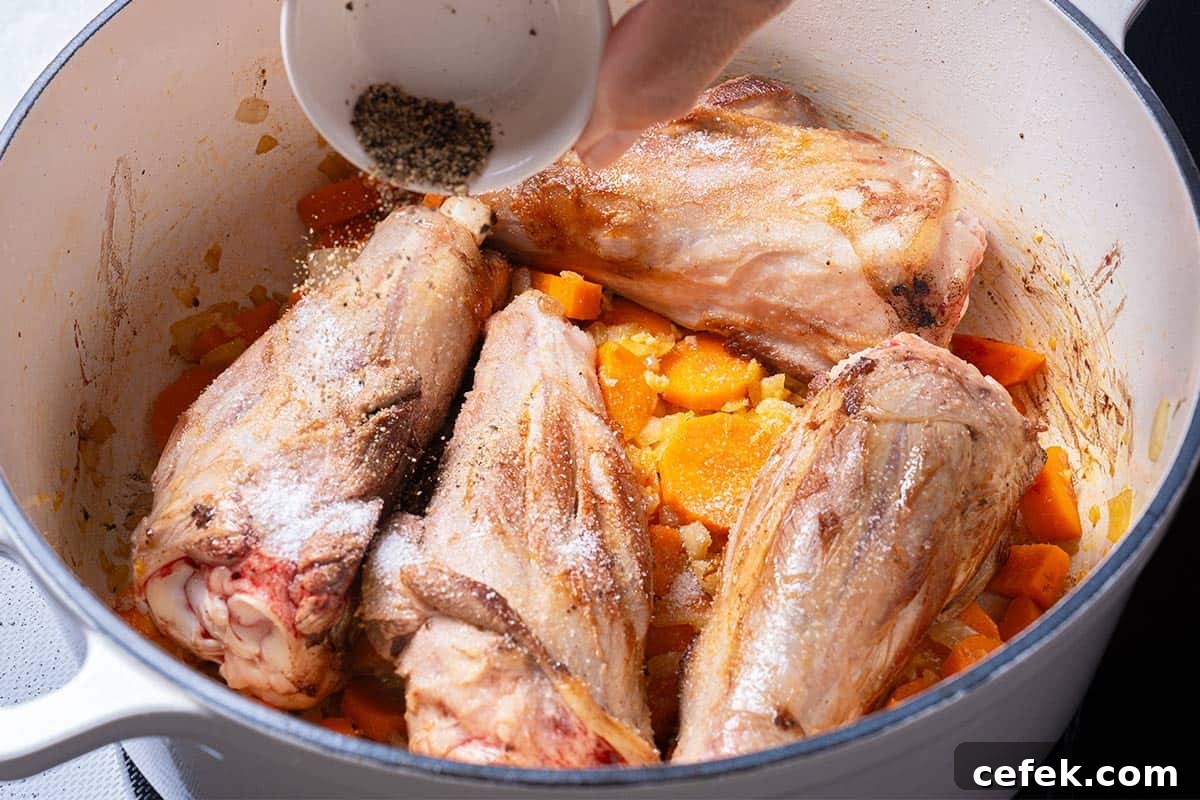 carrots, diced onion  and lamb shanks in a blue pot being sprinkled with salt and pepper