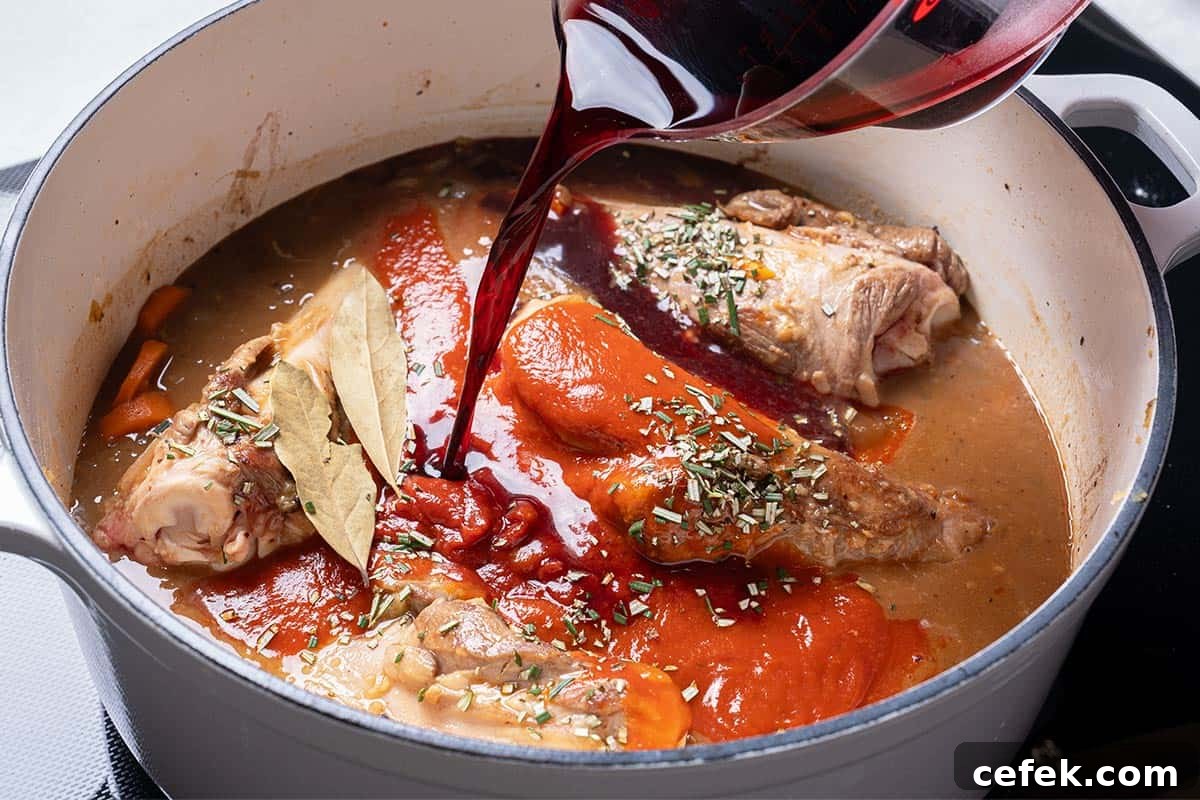 carrots, diced onion  and lamb shanks and stock in a blue pot with wine being poured in