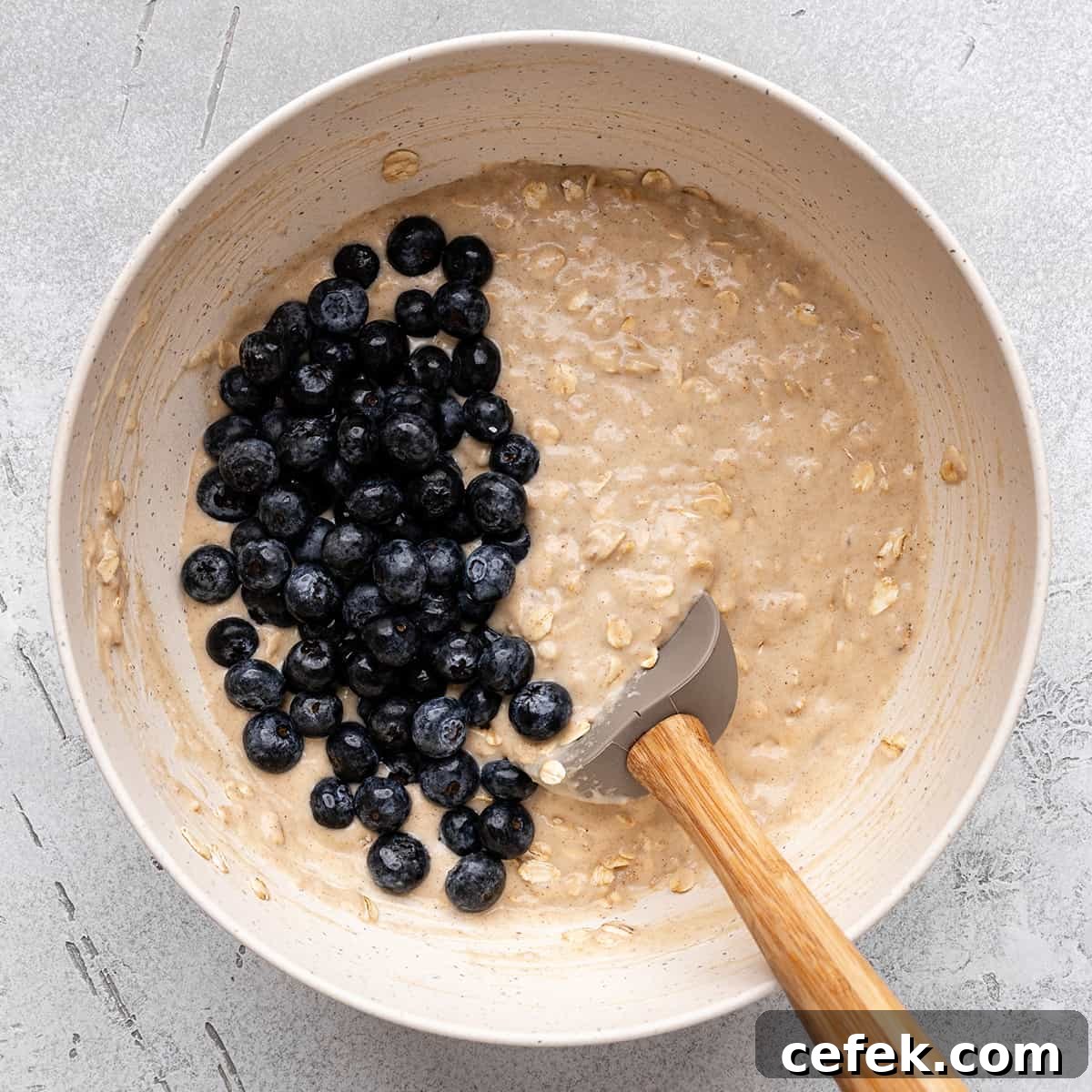 blueberries added to the blueberry oatmeal muffin batter in a bowl with a spatula
