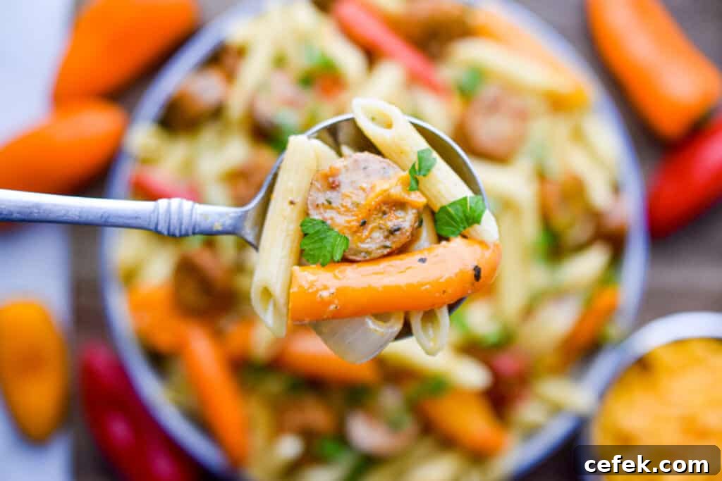 A spoon is lifting the chicken sausage and mini pepper pasta