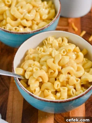 Two bowls of instant pot mac and cheese are on a wooden cutting board with shredded cheese around the bowls.
