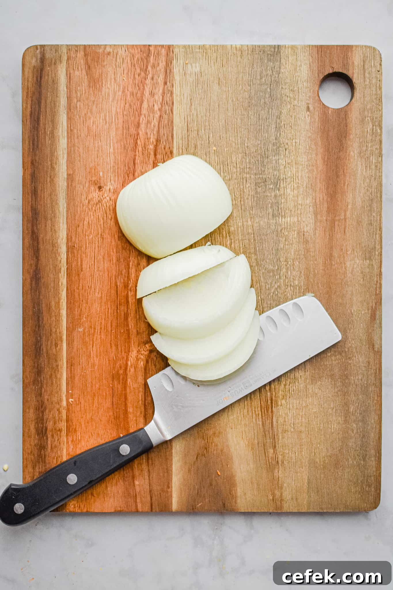 The onions are being sliced on a wooden cutting board