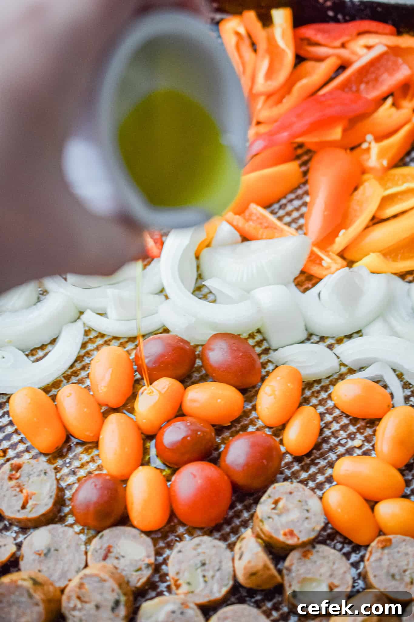 Olive oil is being drizzled over the vegetables and chicken sausage