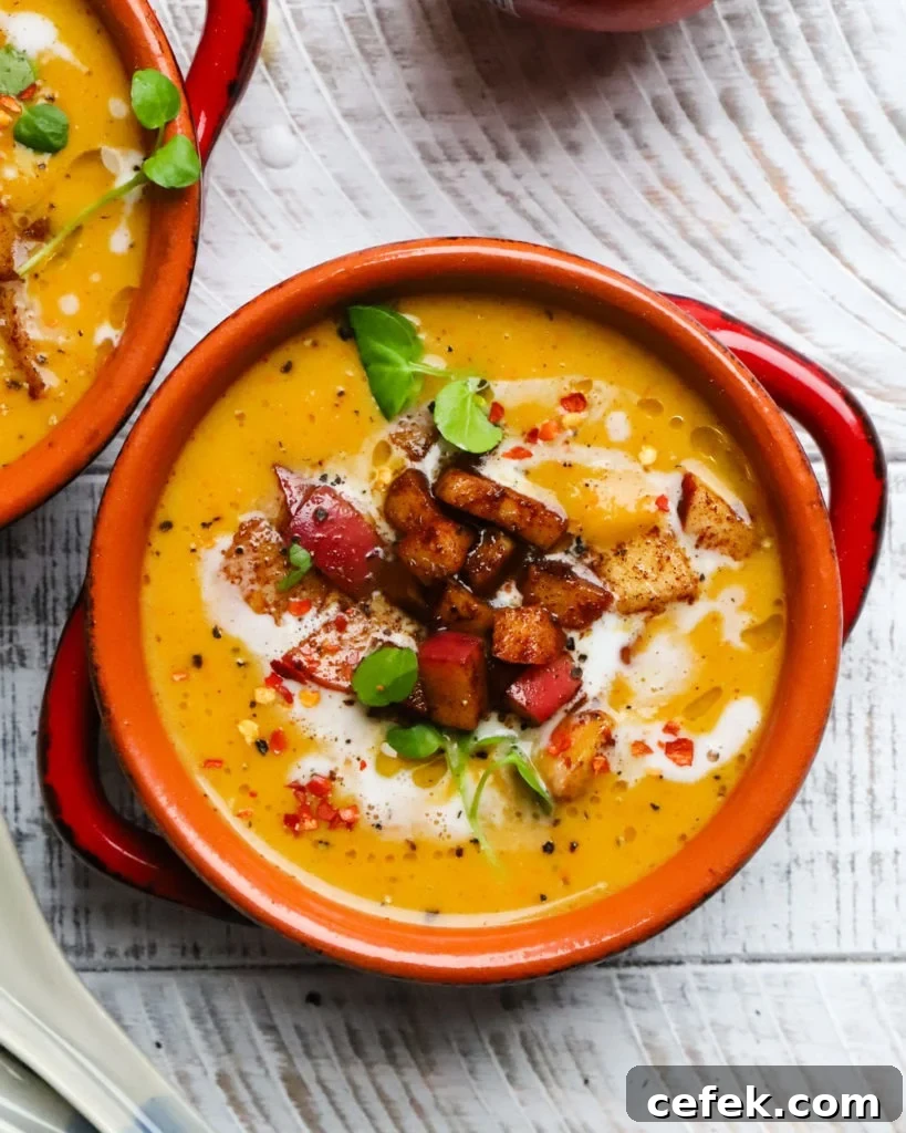 Bowl of creamy butternut squash soup garnished with croutons and herbs on table.