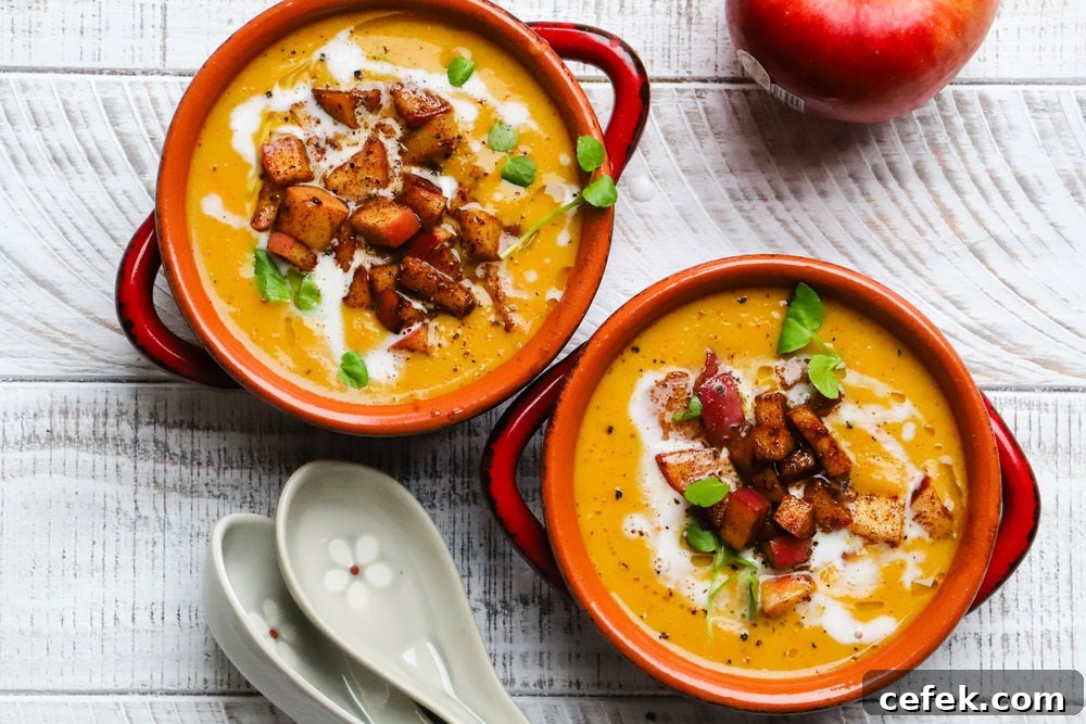 Two bowls of butternut squash soup topped with diced apples and herbs.
