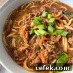 close up shot of beef udon soup in a white bowl garnished with green onion