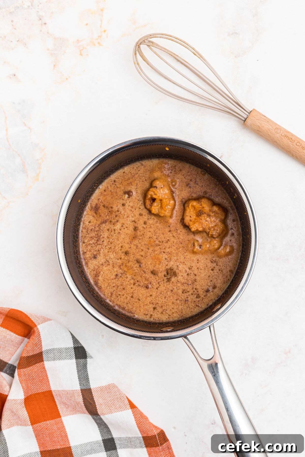Milk, pumpkin, and other ingredients mixed together in a small saucepan with a whisk on the table.