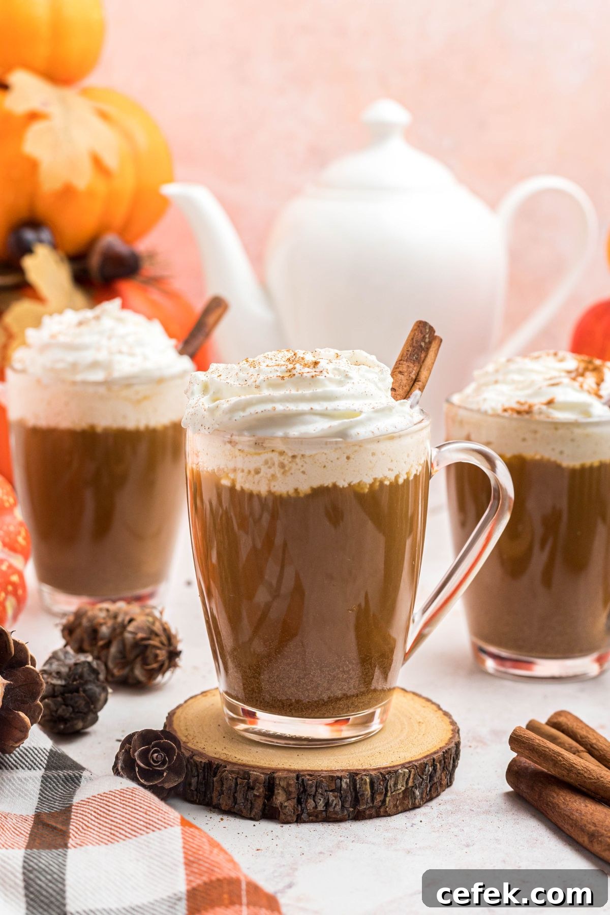 Cups of coffee topped with whipped cream, in front of white pot, on a marble board.
