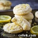 Side shot of a stack of lemon cookies with a half eaten cookie layered in front with a slice of lemon in the background.