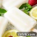 Side shot of lemonade popsicles on a glass plate with mint, lemon slices, and strawberries scattered around.