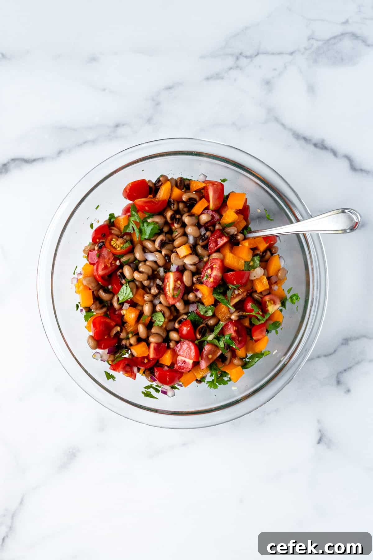 Mixing black eyed pea salad in a glass mixing bowl.