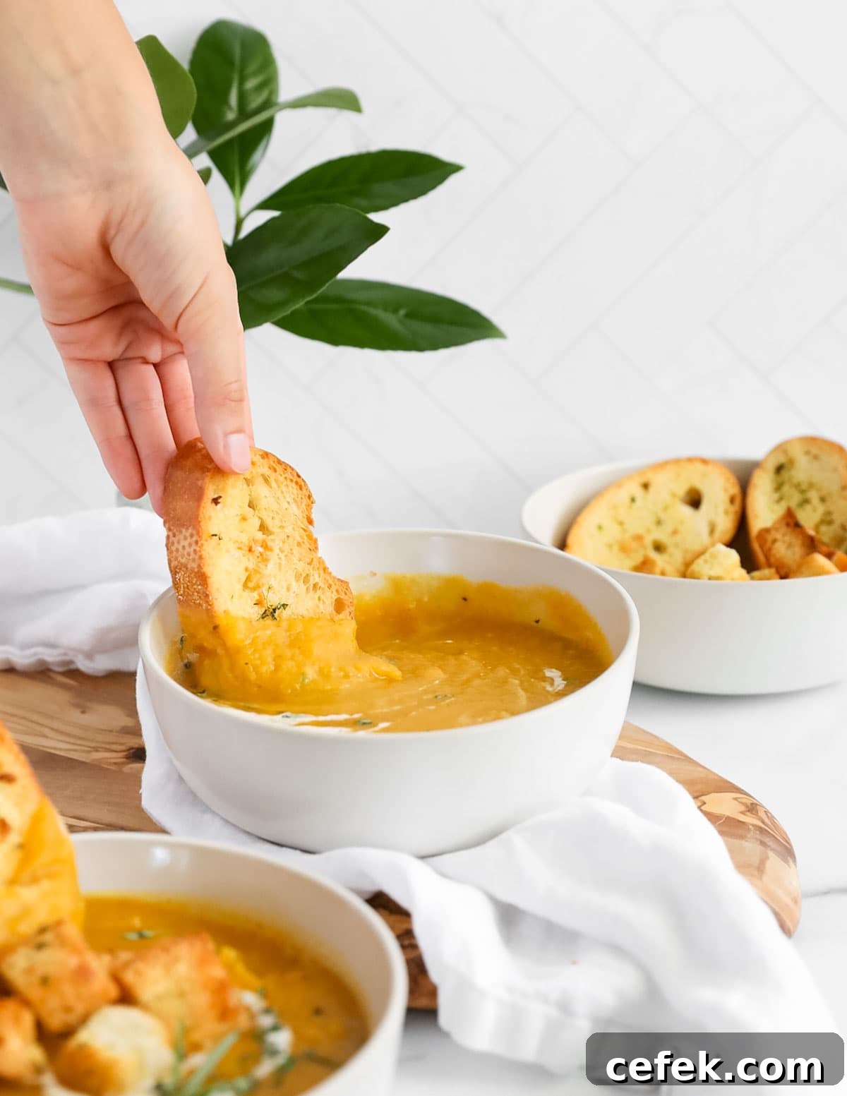A hand dipping a piece of bread into a bowl of orange soup.