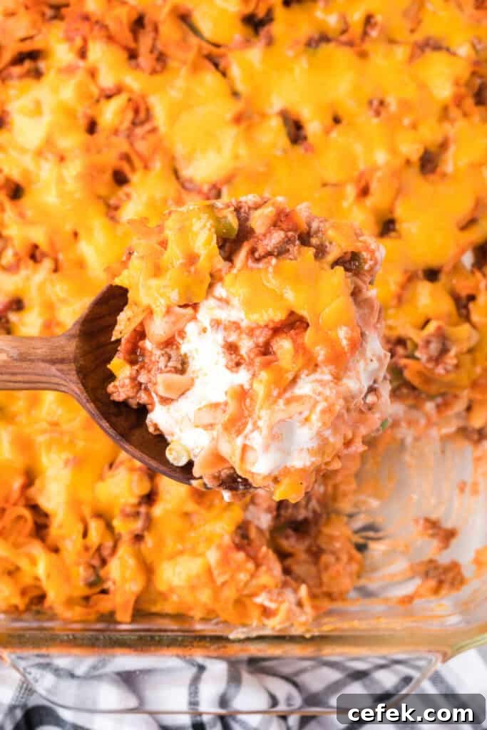spoon lifting a serving of beefy sour cream noodle bake showing layers of meat, noodles, and creamy filling