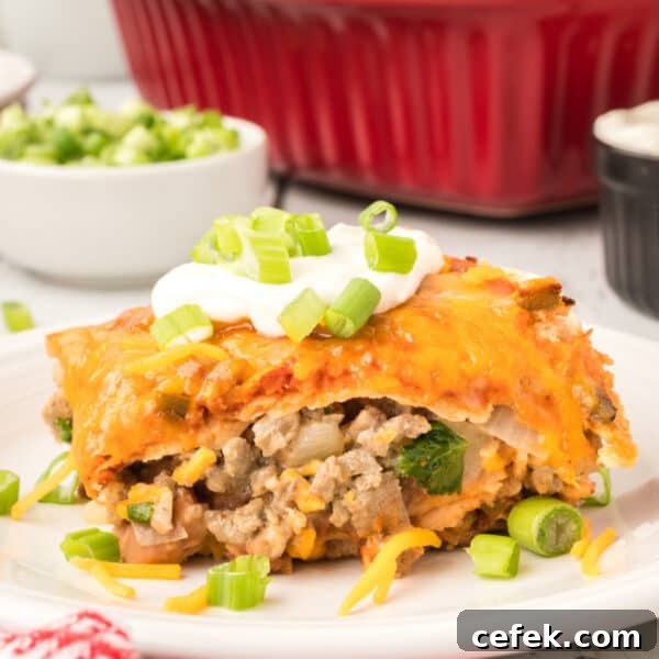 square image of beef and bean enchilada casserole slice topped with sour cream and green onions on a plate