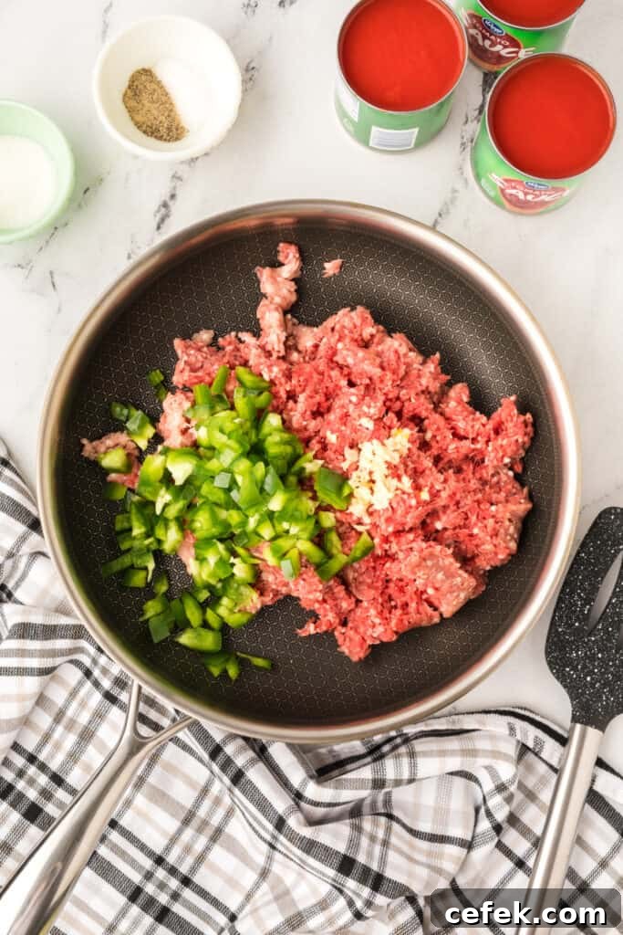 raw ground beef with chopped green pepper and minced garlic in a skillet before cooking
