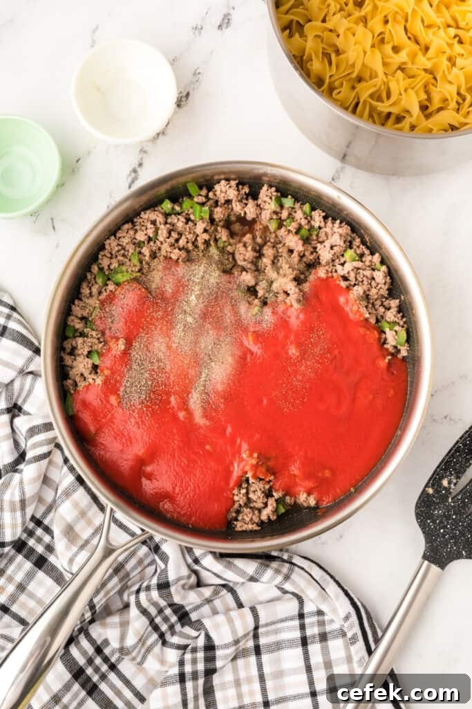 ground beef mixture in skillet with tomato sauce and seasonings added on top
