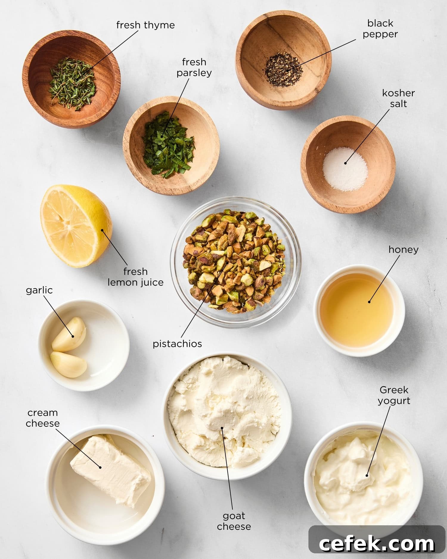 Marble surface with ingredients to make goat cheese dip including pistachios, herbs, honey, cream cheese, goat cheese, and more.