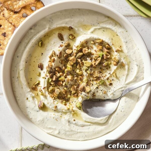 Bowl with whipped goat cheese with pistachios and honey on top with spoon scooping up serving.