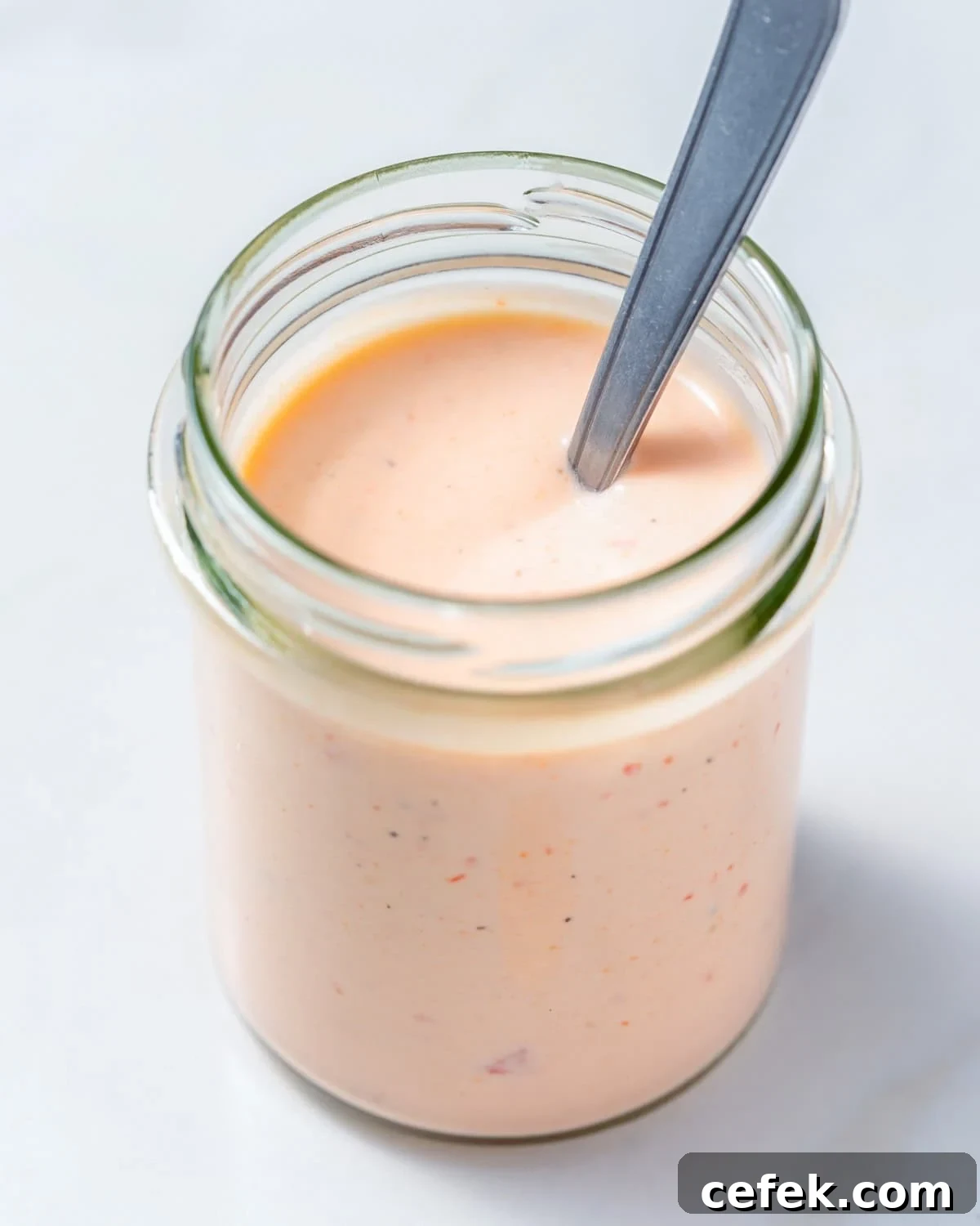 A jar with bang bang sauce with a spoon in the jar.