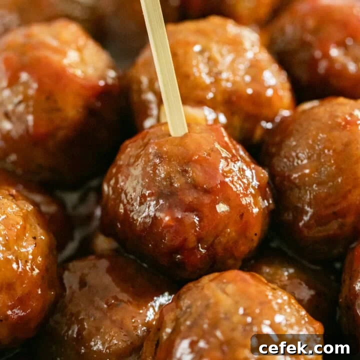 A close up image of a bowl of meatballs in BBQ with a toothpick in the focus meatball.