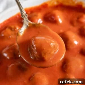 A spoon holding up a porcupine meatball and sauce over the pan of them.