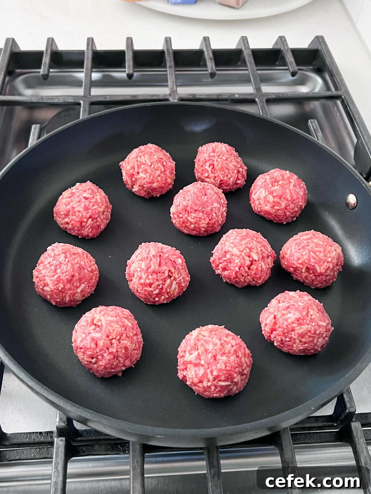 Raw meatballs in a large pan on the stove.