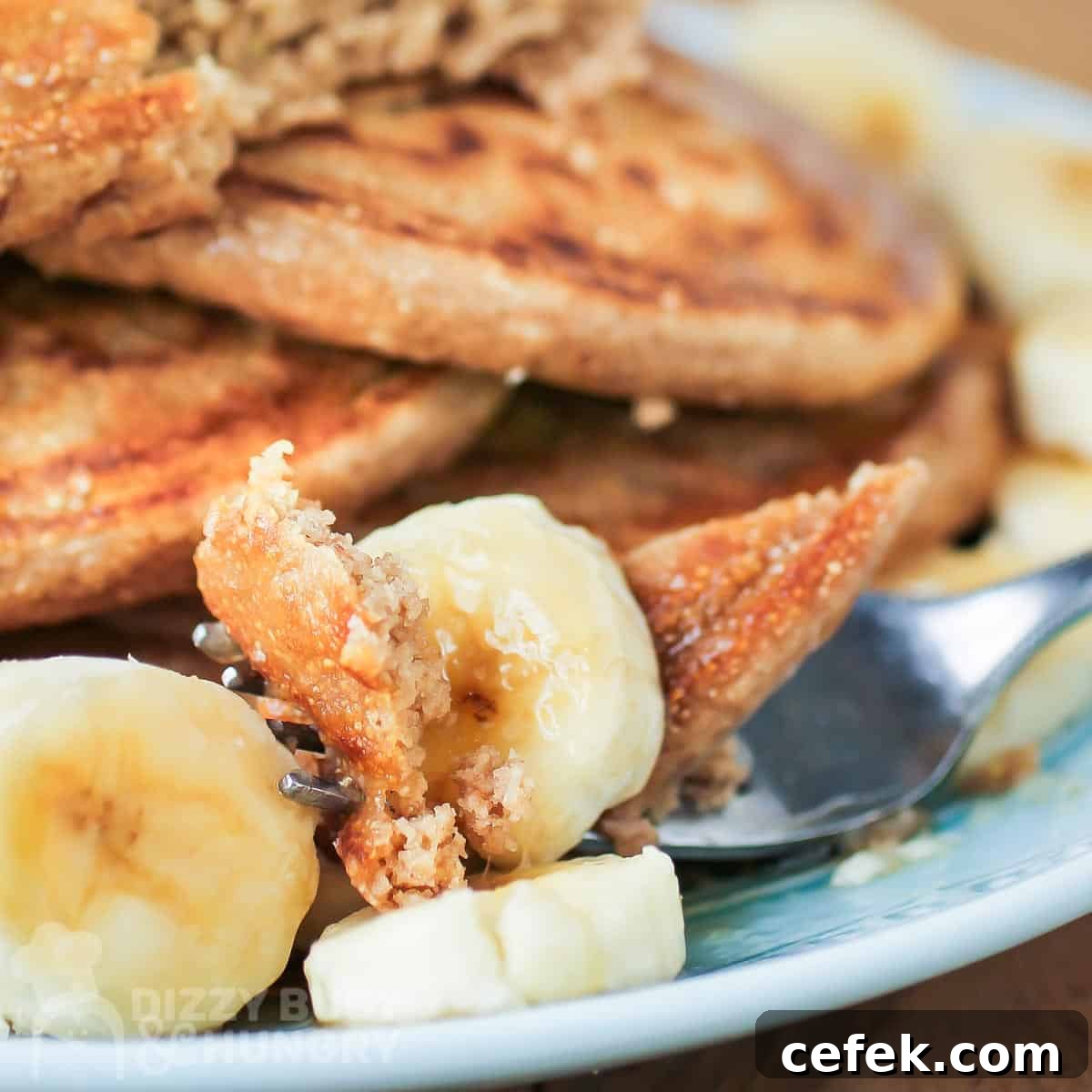 Close up side shot of a fork picking up pieces of pancake and banana on a blue plate.