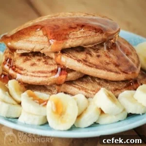 Close up side shot of multiple pancakes stacked on each other with syrup drizzled on them and bananas on the side all on a light blue plate.