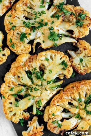 Roasted cauliflower steaks sprinkled with fresh parsley on a baking sheet.