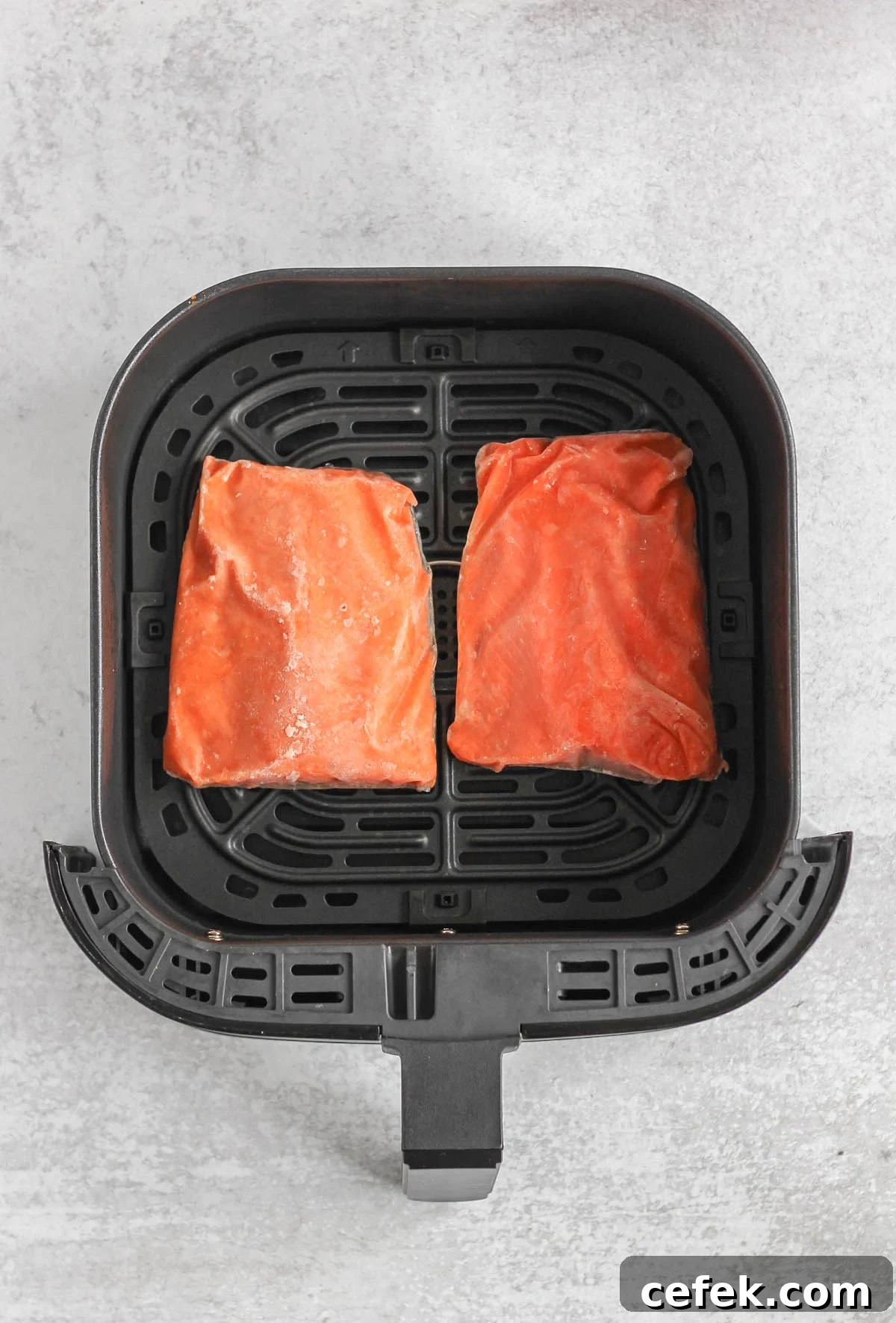 Frozen salmon fillets in an air fryer basket.