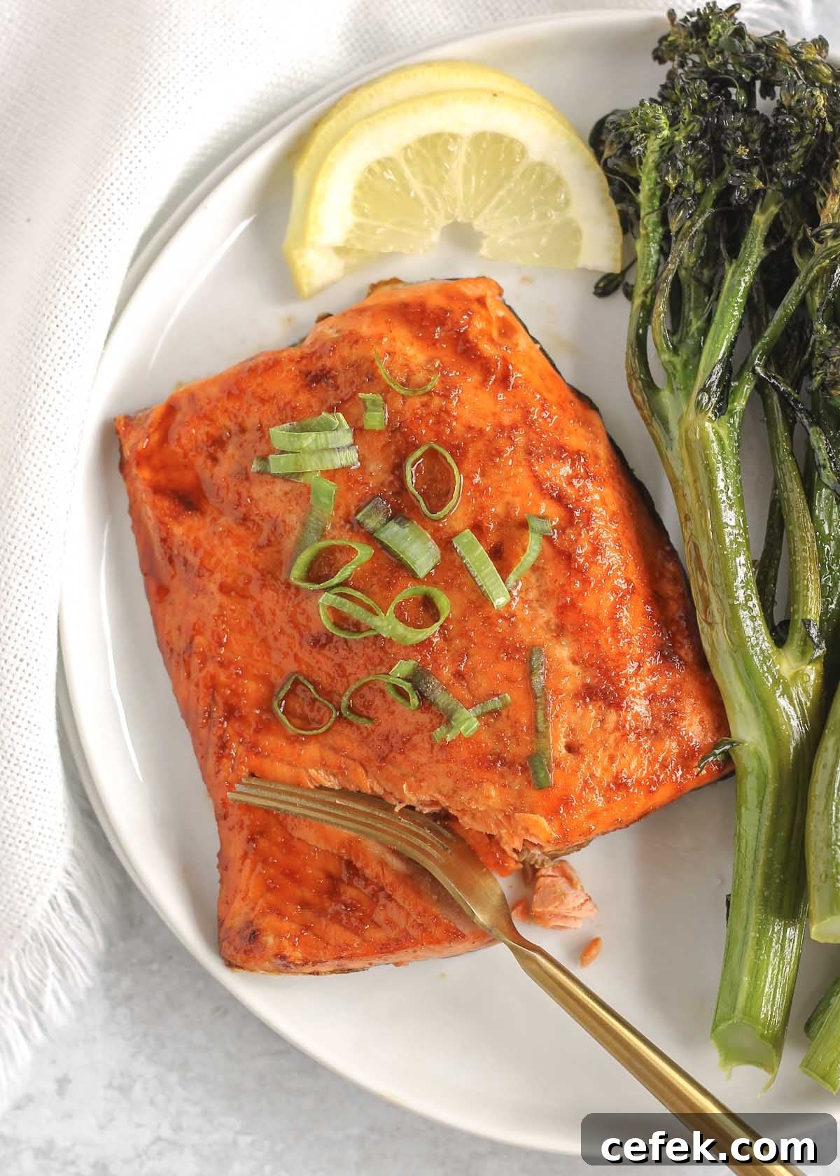 A fork cutting into a salmon fillet on a plate with a side of broccolini and lemon.