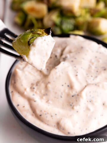 A black bowl with a white sauce and Brussels sprout being dumped in it.